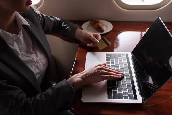 Cropped view of businesswoman working credit card and laptop in aircraft during business trip — Stock Photo