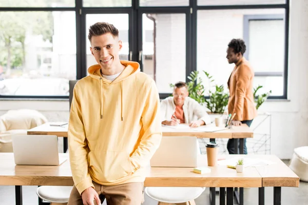 Молодий бізнесмен посміхається на камеру, стоячи біля багатокультурних колег в офісі — стокове фото