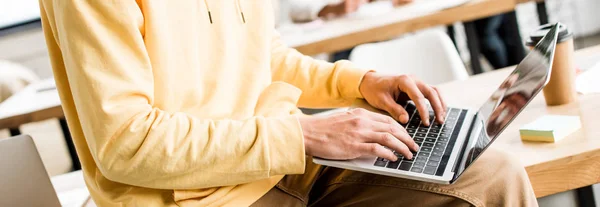 Обрезанный вид молодого бизнесмена, работающего на ноутбуке в офисе, панорамный снимок — стоковое фото