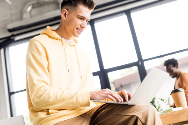 Jeune homme d'affaires souriant tout en utilisant un ordinateur portable au bureau — Photo de stock
