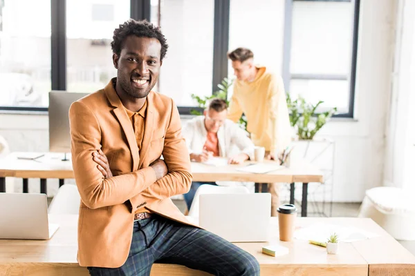 Молодой африканский американский бизнесмен улыбается в камеру, сидя за столом в офисе — стоковое фото