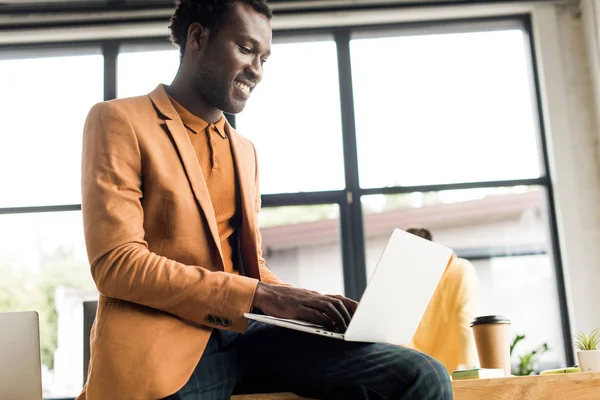 Lächelnder afrikanisch-amerikanischer Geschäftsmann am Schreibtisch sitzend und mit Laptop — Stockfoto