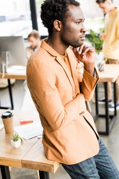 Nachdenklicher afrikanisch-amerikanischer Geschäftsmann schaut weg, während er im Büro in der Nähe von Kollegen steht — Stockfoto