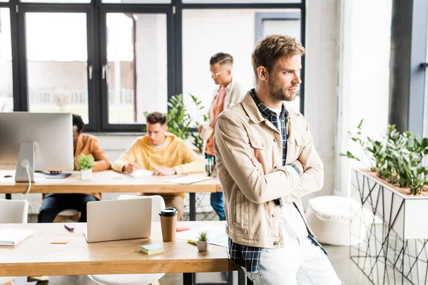 Nachdenklicher Geschäftsmann schaut weg, während multikulturelle Kollegen im Büro arbeiten — Stockfoto