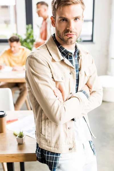 Jungunternehmer blickt mit verschränkten Armen im Büro in die Kamera — Stockfoto