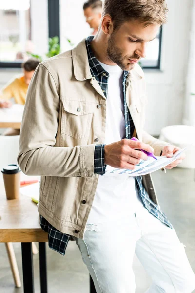 Jeune homme d'affaires analysant des graphiques et des graphiques près de collègues travaillant dans le bureau — Photo de stock