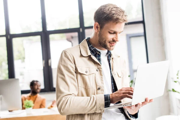 Joven hombre de negocios sonriendo mientras usa el ordenador portátil en la oficina - foto de stock