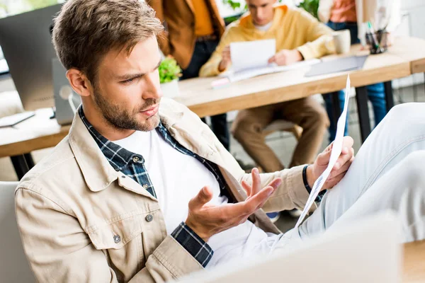 Selektiver Fokus junger Geschäftsleute bei der Analyse von Dokumenten in der Nähe von Kollegen, die im Büro arbeiten — Stockfoto