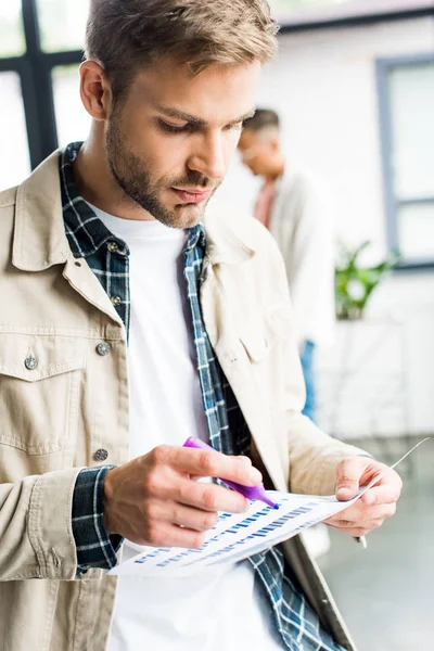 Jungunternehmer schaut im Büro auf Papier mit Diagrammen und Diagrammen — Stockfoto