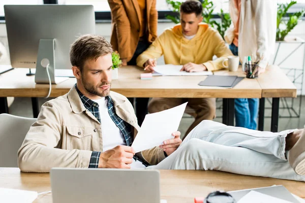 Young businessman sitting with legs on desk near colleagues working in office — Stock Photo