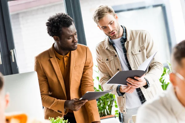 Enfoque selectivo de jóvenes empresarios multiculturales que buscan en carpetas en el cargo - foto de stock