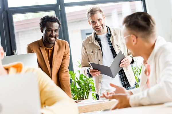 Selective focus of young multicultural businessmen talking and smiling in office — Stock Photo