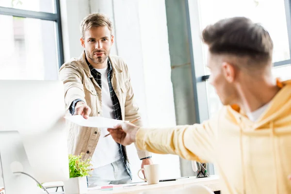 Selektiver Fokus eines jungen Geschäftsmannes, der seinem Amtskollegen Papier schenkt — Stockfoto