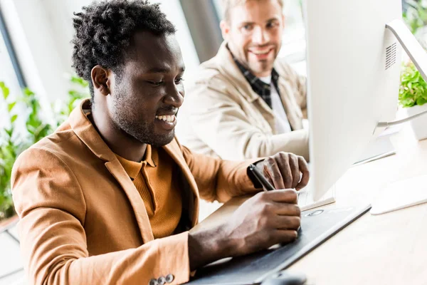 Selective focus of african american businessman using tablet while sitting near colleague in office — Stock Photo