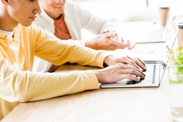 Abgeschnittene Ansicht eines jungen Geschäftsmannes mit Laptop, während er in der Nähe eines Kollegen im Büro sitzt — Stockfoto