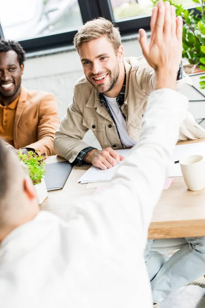 Jovens, empresários alegres dando alta cinco enquanto sentado no local de trabalho no escritório — Fotografia de Stock