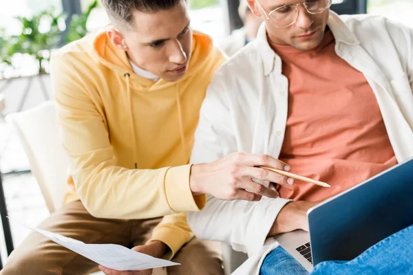 Young businessman pointing with pencil at laptop in hands of colleague — Stock Photo