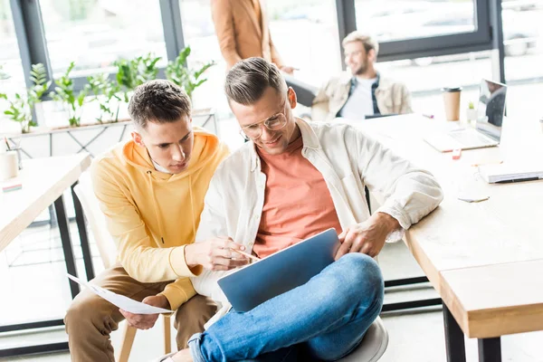 Jeunes gens d'affaires regardant ordinateur portable tout en travaillant ensemble dans le bureau — Photo de stock