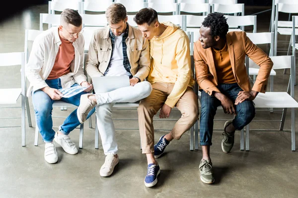 Cuatro jóvenes empresarios multiculturales discutiendo el proyecto de startup mientras están sentados en la sala de conferencias - foto de stock