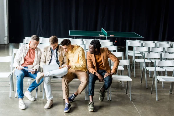 Quattro giovani imprenditori multiculturali che discutono del progetto di startup mentre sono seduti in sala conferenze — Foto stock