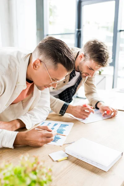 Zwei junge Geschäftsleute analysieren Aufsätze mit Diagrammen und Diagrammen, während sie gemeinsam im Büro an einem Startup-Projekt arbeiten — Stockfoto