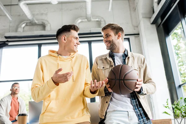 Joven hombre de negocios alegre celebración de voleibol mientras habla con su colega en el cargo - foto de stock