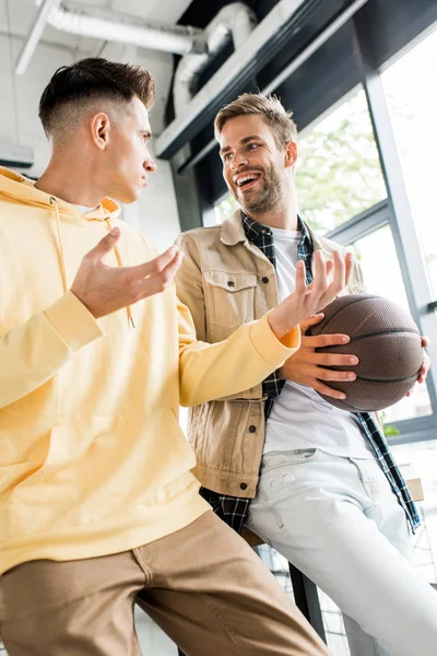 Joven empresario gesticulando mientras habla sonriente colega sosteniendo voleibol - foto de stock