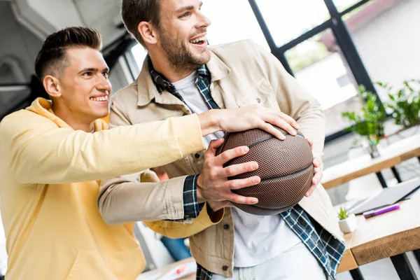 Jeune homme d'affaires joyeux prenant le volley-ball des mains d'un collègue souriant au bureau — Photo de stock