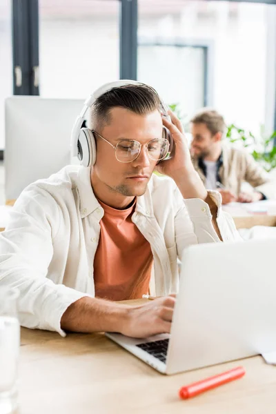 Joven empresario pensativo utilizando el ordenador portátil mientras está sentado en los auriculares - foto de stock