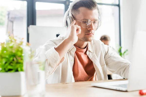 QUIIV, UCRÂNIA - 1 DE AGOSTO DE 2019: foco seletivo de empresário atencioso sentado em fones de ouvido e usando laptop no escritório — Fotografia de Stock
