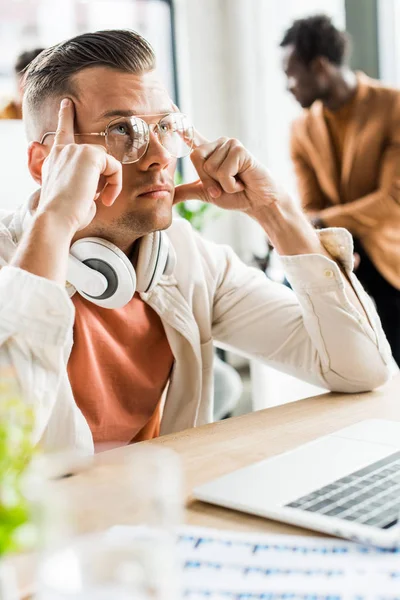 Jeune homme d'affaires coûteux levant les yeux tout en étant assis avec casque sur le cou — Photo de stock