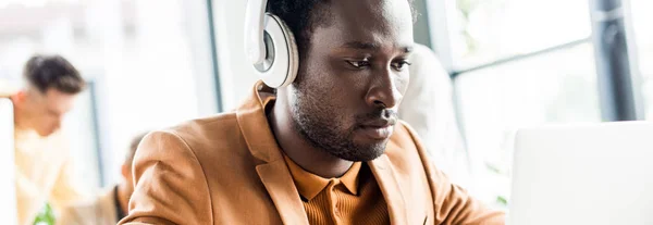 Plan panoramique de beau homme d'affaires afro-américain dans les écouteurs travaillant dans le bureau — Photo de stock