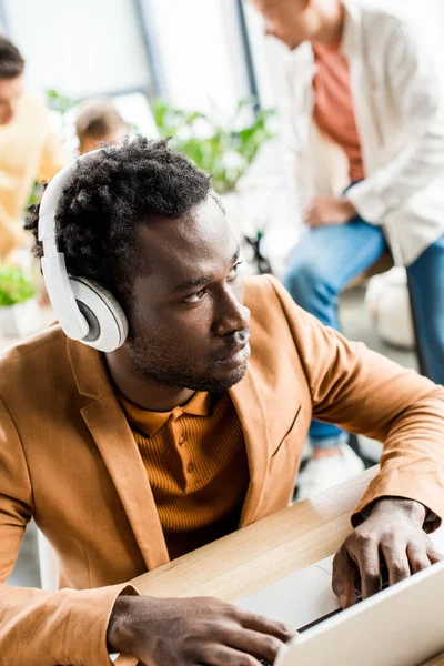Grave homme d'affaires afro-américain dans les écouteurs à l'aide d'un ordinateur portable au bureau — Photo de stock