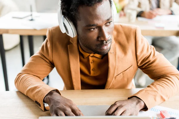 Задумливий афроамериканський бізнесмен в навушниках, використовуючи ноутбук в офісі — стокове фото