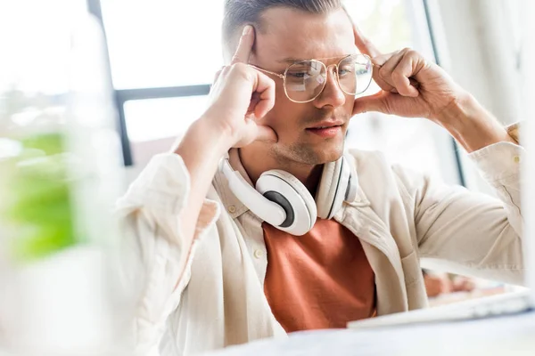 Selektiver Fokus des nachdenklichen Geschäftsmannes, der mit Kopfhörern am Hals am Arbeitsplatz sitzt — Stockfoto