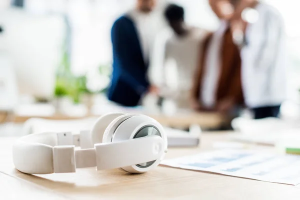 Selektive Fokussierung der Kopfhörer auf den Schreibtisch in der Nähe von Geschäftsleuten, die am Arbeitsplatz im Büro stehen — Stockfoto