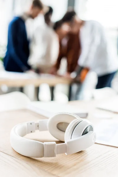 Selektive Fokussierung der Kopfhörer auf den Schreibtisch in der Nähe von Geschäftsleuten, die am Arbeitsplatz im Büro stehen — Stockfoto