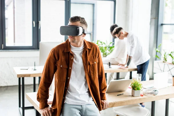 Jovem empresário usando fones de ouvido vr enquanto colegas multiculturais que trabalham no escritório — Fotografia de Stock