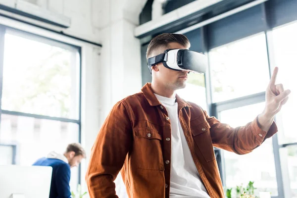 Jeune homme d'affaires toucher quelque chose avec le doigt tout en utilisant un casque de réalité virtuelle au bureau — Photo de stock
