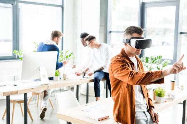 Young businessman using vr headset and touching something with finger while multicultural colleagues working in office — Stock Photo