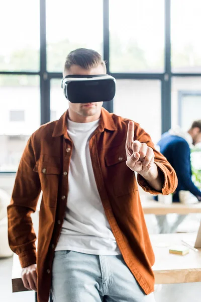 Jeune homme d'affaires toucher quelque chose avec le doigt tout en utilisant un casque de réalité virtuelle au bureau — Photo de stock