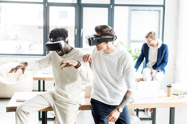 Dos alegres colegas multiculturales usando auriculares vr en la oficina - foto de stock