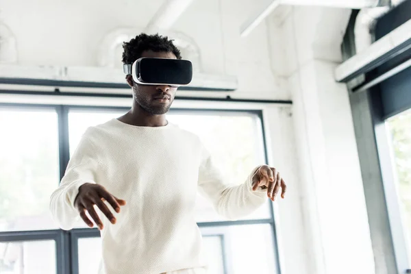 Joven hombre de negocios afroamericano usando auriculares de realidad virtual en la oficina - foto de stock