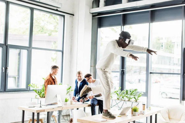 Афріканський американський бізнесмен, який користується вусовим навушником і стоїть на столі в той час як колеги працюють в офісі — стокове фото