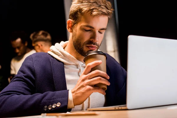 Exhausted businessman drinking coffee to go while working at night in office — Stock Photo