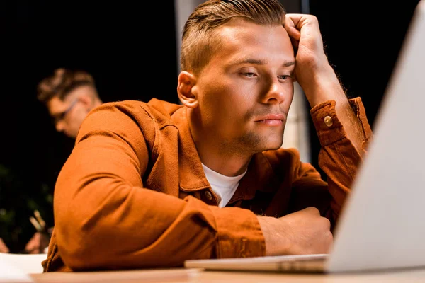 Junger, erschöpfter Geschäftsmann schaut nachts im Büro auf Laptop — Stockfoto