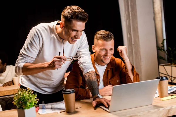 Fröhliche Geschäftsleute, die nachts im Büro auf Laptop schauen — Stockfoto