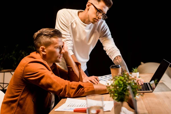 Young businessman standing near tired colleague working at laptop at night — Stock Photo