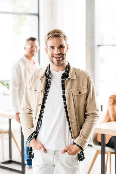 Cheerful, young businessman standing with hands in pockets and smiling at camera — Stock Photo