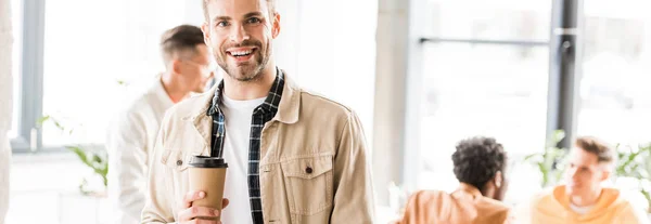 Panoramic shot of young businessman holding coffee to go and smiling at camera — Stock Photo